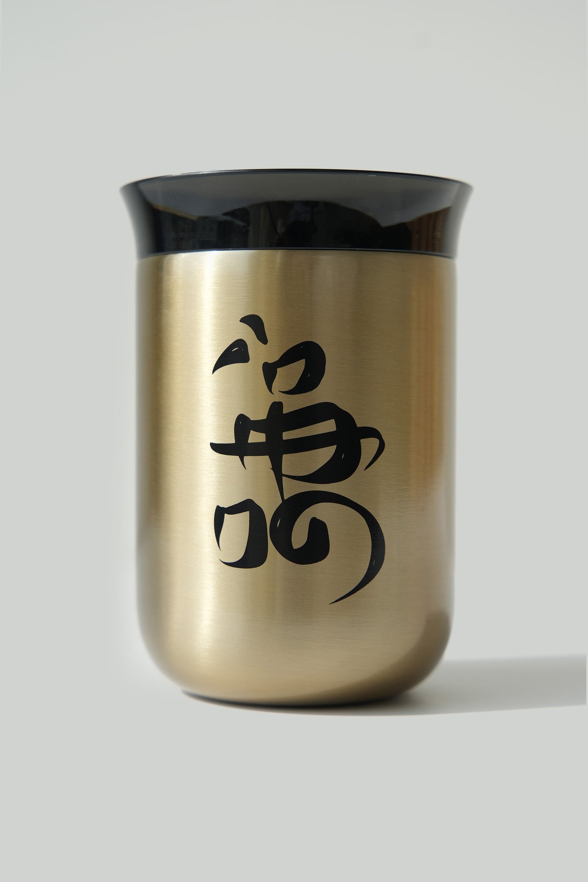 A gold ceramic cup with a black lid and Arabic calligraphy script on the side.